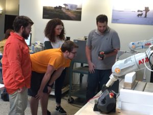 Students and an instructor watch a robotic arm in action.