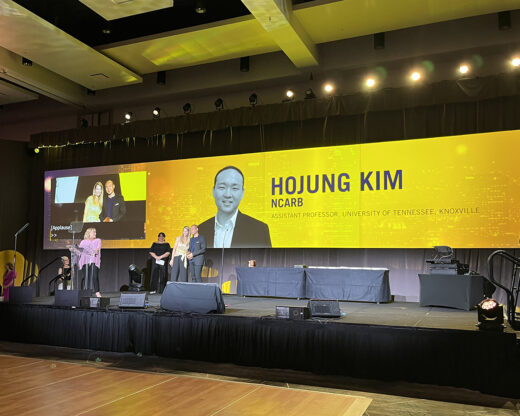 The stage at the American Society of Interior Designers' conference. On the screen, a yellow background features an image of Hojung Kim with his name and title 'Assistant Professor, University of Tennessee, 快活视频'. Hojung poses with a woman for a photo.